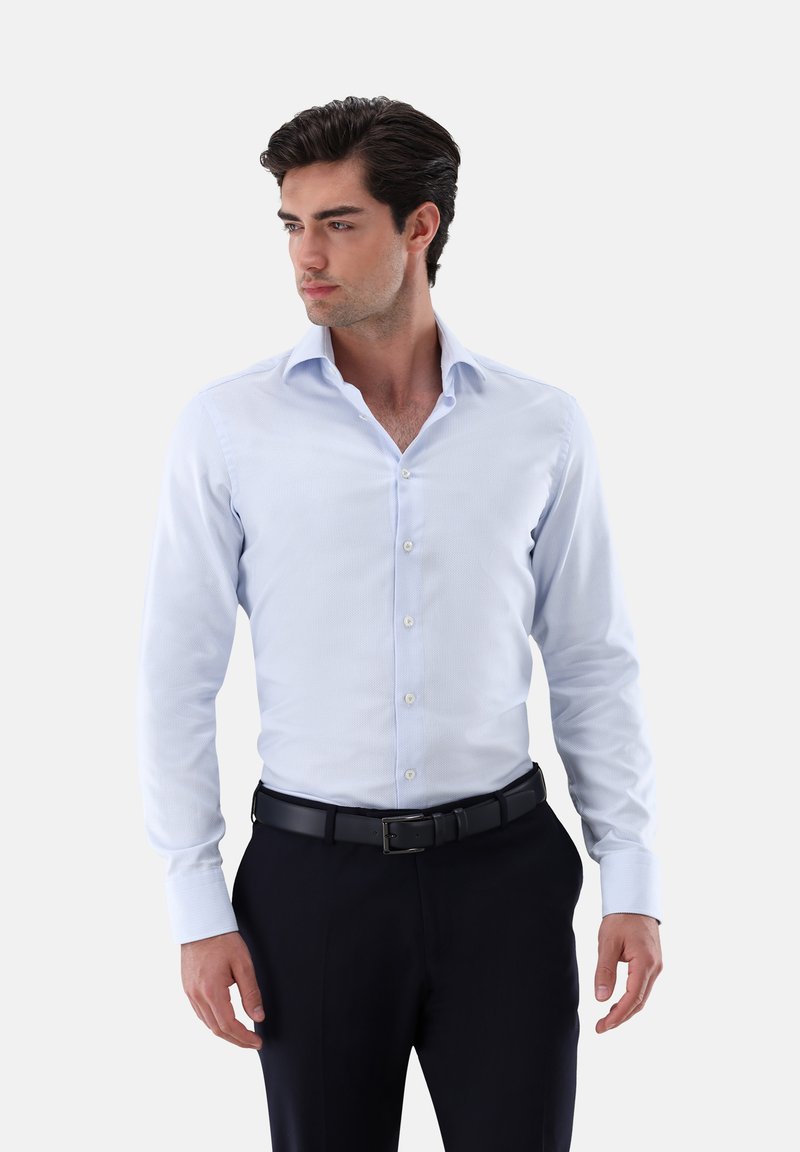 Himmelblaues Hemd mit knöpfbarem Kragen, langen Ärmeln und subtiler Textur. Getragen mit dunklen Hosen und einem schwarzen Gürtel.
