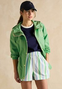 Zaļa viegla lietus jaka ar elastīgām piedurknēm un zelta akcentiem, tumši zila košer piedurkņu krekls un svītrainas bikses zilās un zaļās tonās.