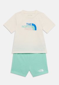 Camiseta de algodón crema de manga corta con logo multicolor; pantalones cortos de algodón verde menta a juego con detalle del logo. Conjunto cómodo y casual.