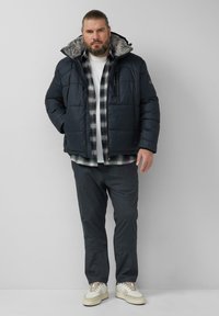 Gewatteerd zwart jack met een capuchon gevoerd met bont, gedragen over een geruit flanellen overhemd en een wit T-shirt, gecombineerd met een donkere broek en witte sneakers.