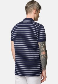 Granatowa koszulka polo z białymi poziomymi paskami, krótkimi rękawami i klasycznym kołnierzykiem; posiada logo na górnej części pleców. Gładka bawełniana tekstura.
