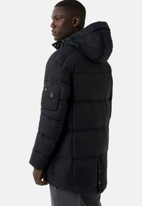 Schwarze Daunenjacke mit Kapuze, die über gesteppte Bereiche, eine Reißverschlusstasche am Ärmel und einen leicht längeren Rückensaum verfügt.