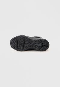 Sola de sapato atlético preto com piso texturizado e logotipo da Nike, vista pela parte inferior sobre um fundo simples.