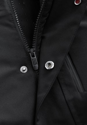 Sort isoleret jakke med frontlynlås, trykknapper og glat stoftstruktur med subtile perforeringer for åndbarhed.