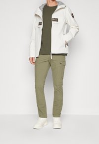 White lightweight jacket with gray lining, two chest pockets, paired with an olive green crew-neck shirt and olive cargo pants. White sneakers.