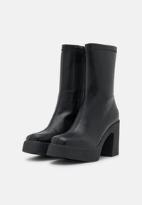 Bottes basses en cuir noir à finition lisse, avec un talon haut et épais texturé et une fermeture éclair latérale pour un enfilage facile.