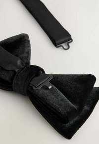 Black velvet bow tie with satin strap, featuring a smooth texture and a black metal clasp detail. The design is classic and sleek.
