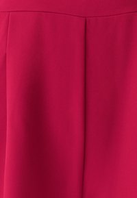 Červené šaty s texturovanou tkaninou a jemným vzorem křížkového šrafování. Obsahují strukturované záhyby vpředu a přiléhavý pas.