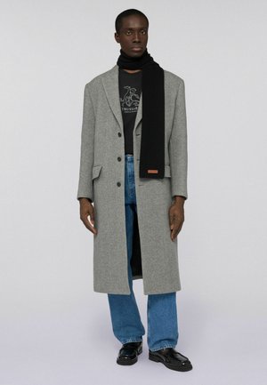 Gray wool overcoat with notch lapels, black ribbed scarf, black T-shirt, and light blue jeans. Black loafers complete the outfit.