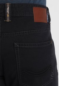 Zwarte spijkerbroeken met een leren patch op de achterkant, contraststiksels en een uniek ontwerp van zakken met gebogen accenten.