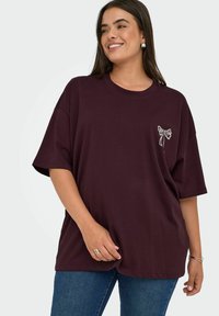 Burgunderfarget oversized T-skjorte laget av bomull, med kort erm og hvit sløyfe broderi på venstre bryst.