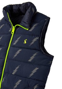 Tummansininen toppaliivi, jossa on korkeakauluksinen malli, kirkkaan keltainen vetoketju ja harmaa salaman kuvio. Kevyt ja vedenpitävä materiaali.