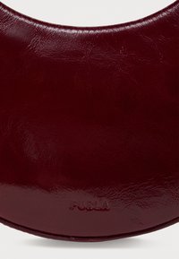 Vīna sarkanā ādas rokassoma ar apļveida dizainu, kurai ir gluda tekstūra un izgriezts "FURLA" logo apakšā.