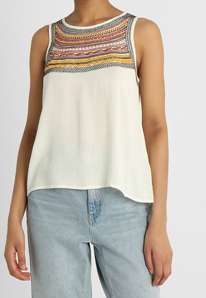 Top blanco sin mangas con canesú bordado en colores naranja, rosa y negro, combinado con vaqueros de mezclilla azul claro.