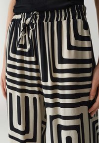 Zwart-witte gestippelde broek met een trekkoord in de taille, met geometrische ontwerpen en een gestructureerde stof.