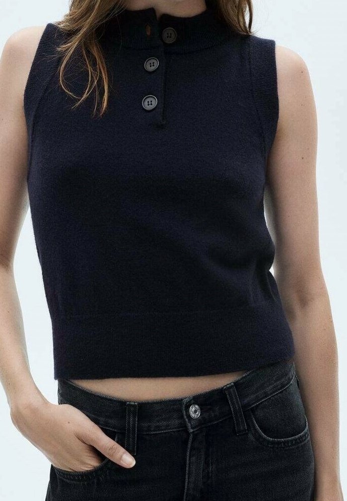 Granatowy dzianinowy top bez rękawów z wysokim kołnierzem i zapięciem na trzy guziki. Charakteryzuje się dopasowanym krojem i miękką teksturą, zestawiony z ciemnymi jeansami.
