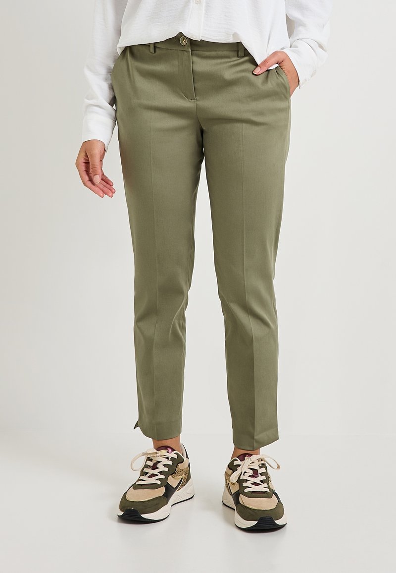 Pantalons taillés vert olive avec une texture lisse, dotés d'une fermeture à bouton, de poches latérales et d'une finition au niveau de la cheville. Portés avec des baskets neutres.