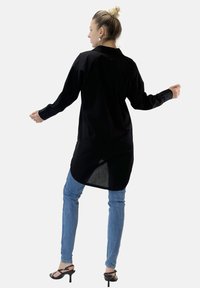 Czarna longsleeve z kołnierzykiem, z zakrzywionym dołem i luźnym krojem, połączona z jasnoniebieskimi wąskimi dżinsami i czarnymi sandałami na obcasie.