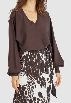 Vrouw die een donkerbruine V-hals trui met ballonmouwen draagt en een hoge taille rok met een zwart-wit abstract bloemmotief.