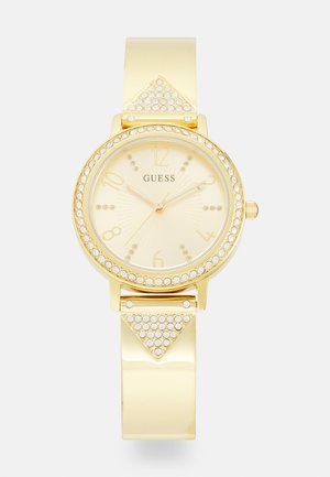 Gold watch with a round face, yellow dial, and crystal accents. Features a glossy band and decorative triangle detail with rhinestones.