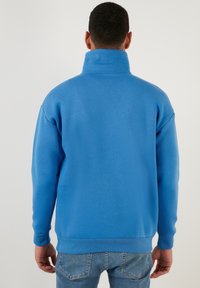 Felpa blu con collo alto, maniche lunghe, polsini a coste e una vestibilità comoda. Realizzata in un morbido tessuto testurizzato.