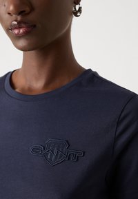 Námornícke modré tričko s okrúhlym výstrihom, na hrudi s vyšitým logom v tmavomodrej farbe. Mäkko hladký bavlnený materiál.