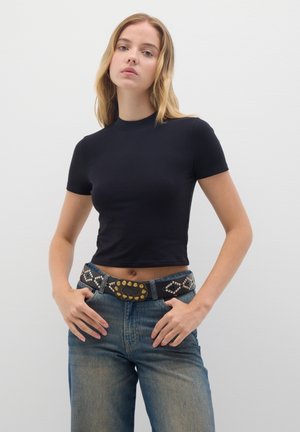 Camisa corta negra de manga corta combinada con jeans de tiro alto azules y un cinturón decorativo con acentos metálicos y patrones de tachuelas.