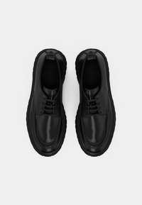 Juodos odinės batai su lygia apdaila, apvaliu pirštu ir storu tekstūruotu padu. Yra raišteliai ir kilpos ant kulno, kad būtų lengva užsidėti.