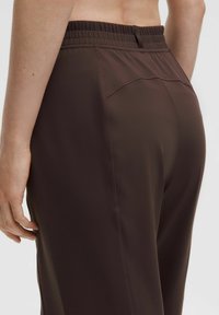 Braune Sporthosen mit einem dehnbaren Bund, glatter Textur und seitlichen Nähten für eine taillierte Passform. Keine sichtbaren Logos oder Muster.