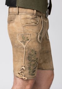 Shorts en cuir de couleur beige clair avec des motifs floraux brodés en vert. Caractéristiques : lacets en bas et plusieurs poches. Texture lisse.