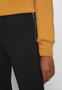 Svarta tights med en dragkedja ficka på sidan och en senapsgul tröja, med ribbad ärm och mjuk textur.