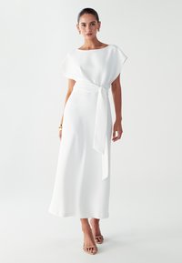 Bijela maxi haljina opuštenog kroja, kratkih rukava i detaljem vezivanja u struku. Glatka tkanina s mekim teksturom, minimalistički dizajn.