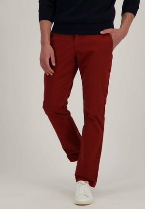 Pantalons en coton chino rouge avec une coupe droite, des poches latérales et une finition soignée. Associés à des sneakers blanches.