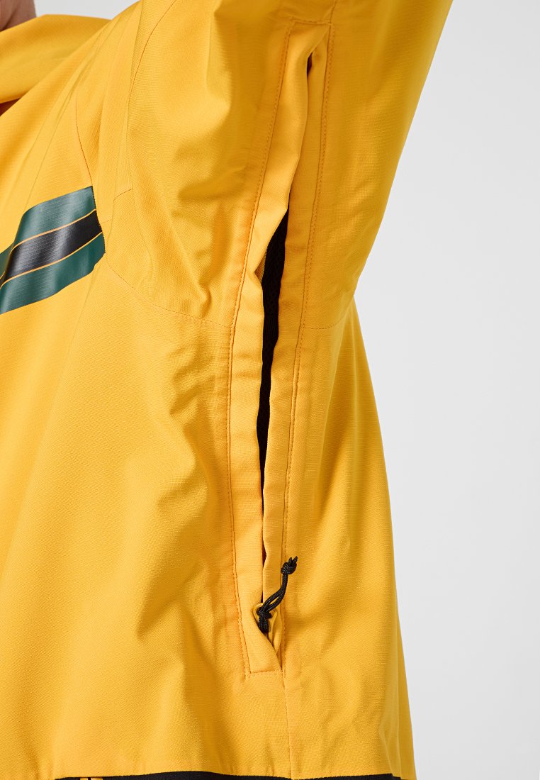 Giacca gialla con tasca laterale con zip, interno nero e striscia di accento verde. Realizzata in tessuto liscio e resistente all'acqua.