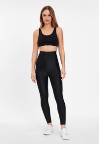 Svart atletisk crop top och höga leggings av slät, stretchig tyg med en figurnära design. Vita sneakers som skor.
