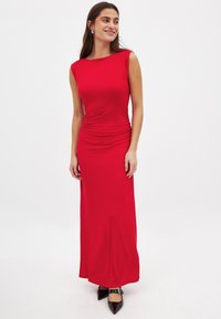 Czerwona, bezrękawna sukienka maxi o gładkiej fakturze i marszczonym boku. Połączona z czarnymi, szpiczastymi butami.