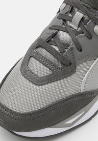 Šedé sportovní tenisky s horní částí z prodyšné síťoviny a semiše, kulatou špičkou, textilními tkaničkami a kontrastními texturovanými akcenty. Odolná gumová podrážka.