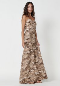 Maxi dress in a beige and brown fern pattern. Features thin straps, a fitted bodice, and a flowing skirt, crafted from lightweight fabric.