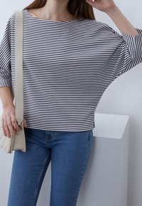 Svart- och vitrandig bred topp med båtkrage, tillsammans med en ljusbeige handväska och blå jeanjackor. Avslappnad, lös passform och textur.