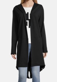 Cárdigan negro con capucha, hecho de una tela suave, con un frente abierto, mangas largas y un bajo curvado. Estampado gráfico blanco debajo.