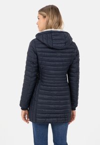 Marine blauwe gewatteerde jas met capuchon, voorzien van verticale stiksels, een tailleverstrakkende ontwerp en een gladde textuur. Achteraanzicht weergegeven.