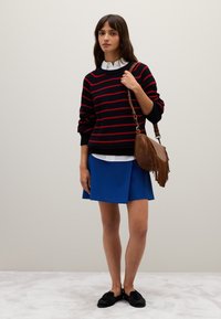 Maglione a strisce black e rosse, gonna blu, borsa a frange marrone e calzature nere. Texture lisce; vestibilità comoda; sovrapposto a una camicia bianca con colletto.