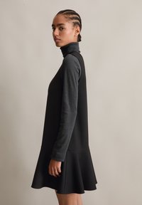 Μαύρο φόρεμα με φουσκωτό σχέδιο, διαθέτει ψηλό λαιμό και μακριά μανίκια. Το ύφασμα έχει υφασμάτινη εμφάνιση με διακριτά σχέδια.