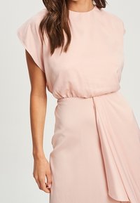 Light pink dress with short, wide sleeves, a gathered waist, and draped fabric detail extending from the side. Smooth, flowing texture.