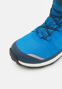 Blue athletic shoe featuring a breathable mesh upper, rubber sole, and contrasting dark blue accents with reflective details.