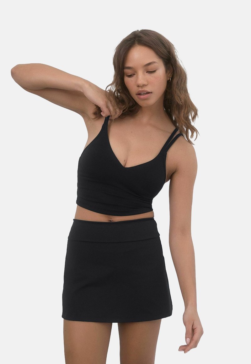 Top corto nero con spalline sottili e scollatura a V profonda, abbinato a una gonna nera coordinata. Tessuto liscio, design aderente, dettagli minimi.