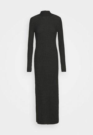Longue robe noire en maille côtelée avec manches longues et col haut s'étendant jusqu'au milieu du mollet sur fond blanc.