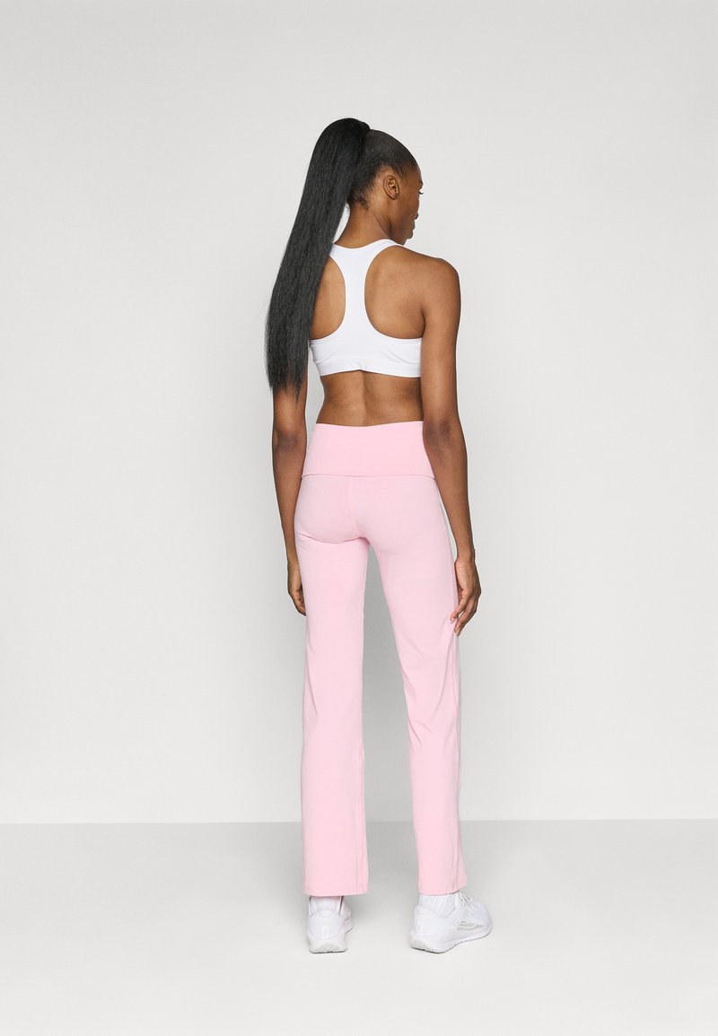 Top sportivo bianco e leggings svasati rosa chiaro, con un alto punto vita e superficie liscia. Modella vista da dietro.