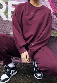 Sudadera burdeos con logo, joggers burdeos a juego y zapatillas en blanco y negro. Tejido texturizado, puños acanalados y corte relajado.
