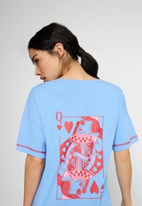 Gaiši zila T-krekla ar lielu sarkano dāmas kārtīm grafiku uz muguras, ar sarežģītām detaļām un sirds motīviem. Īsas piedurknes un brīvs piegriezums.